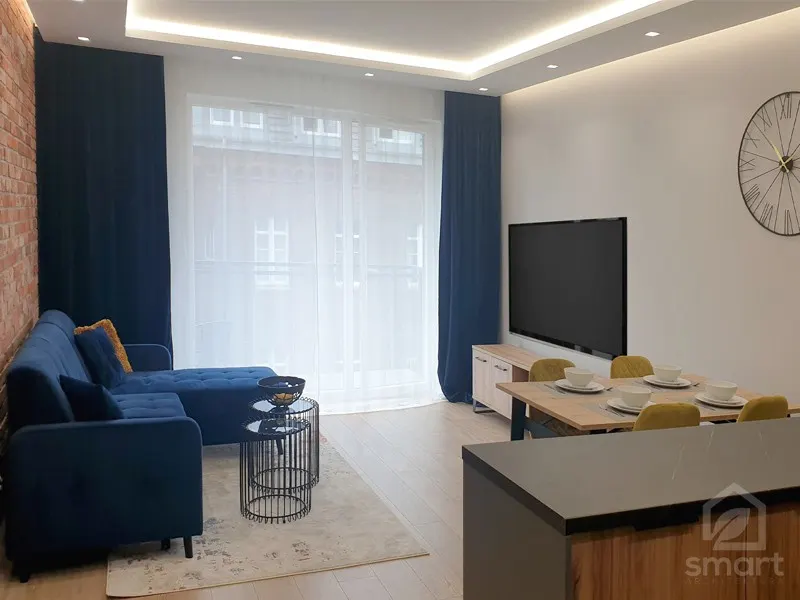 Salon z ceglaną ścianą, granatową sofą narożną, stołem jadalnianym i podświetlanym sufitem