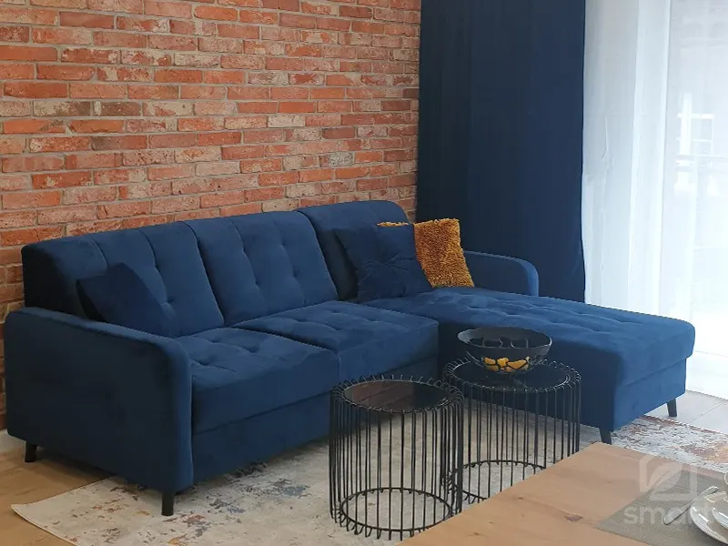 Granatowa sofa narożna na tle ściany z cegły i czarne druciane stoliki kawowe