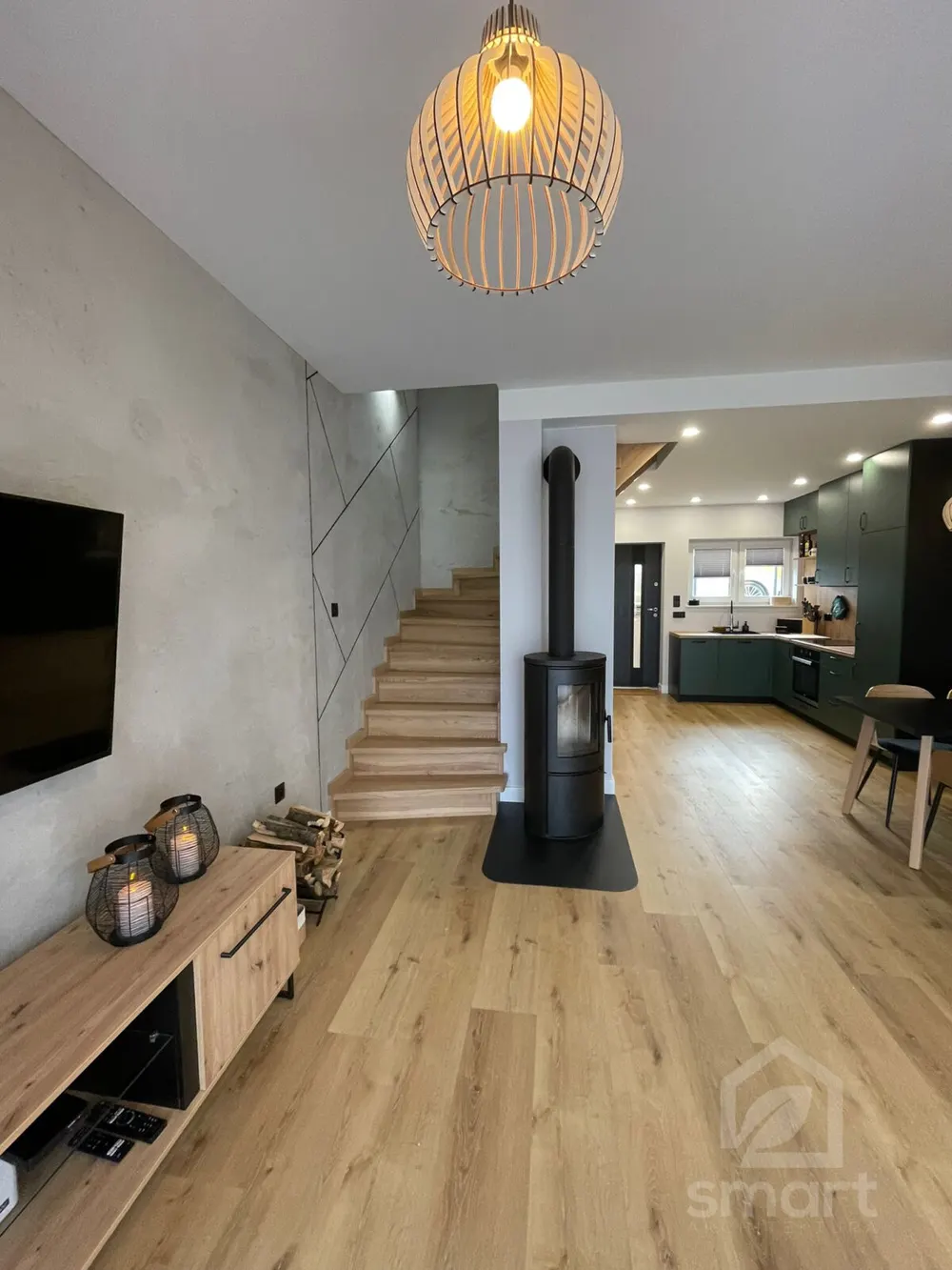 Salon z ażurową drewnianą lampą, betonem dekoracyjnym na ścianie i kozą przy schodach
