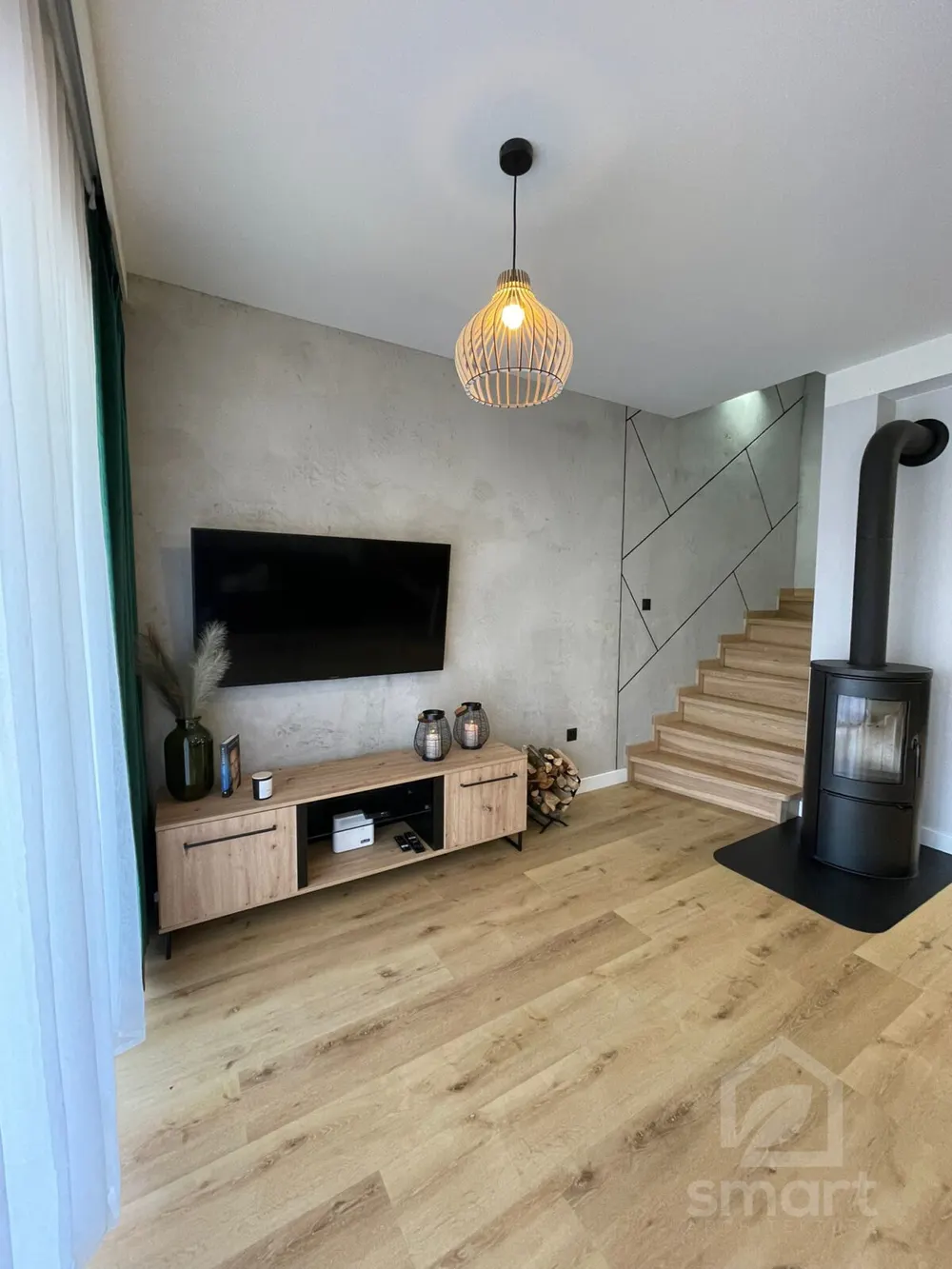 Ściana z betonu dekoracyjnego z telewizorem, drewnianą lampą wiszącą i lampionami na szafce
