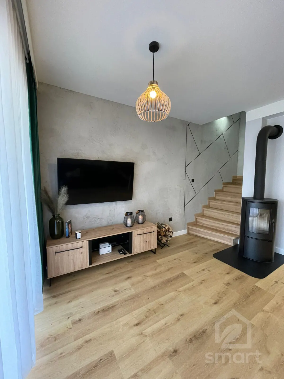 Ściana z betonu dekoracyjnego z telewizorem, drewnianą lampą wiszącą i lampionami na szafce