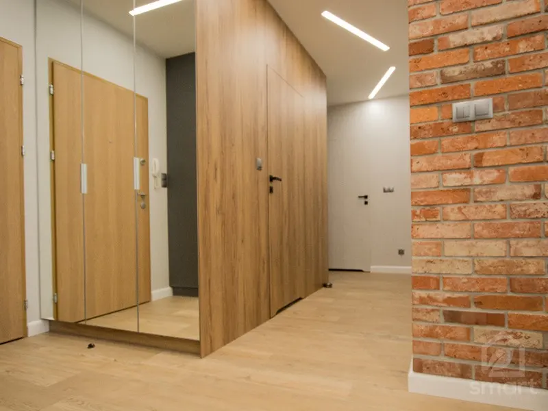 Przedpokój z lustrzaną szafą, zabudową z drewnopodobnych płyt i fragmentem ceglanej ściany