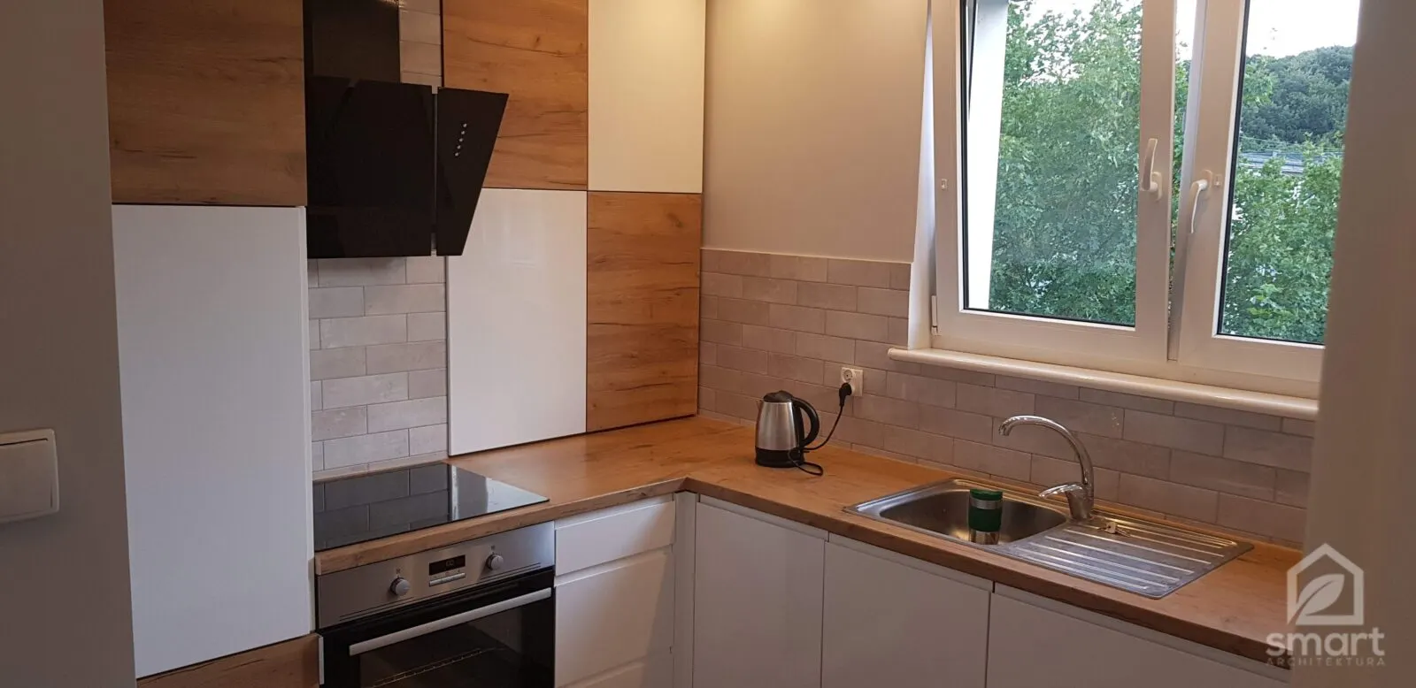 Kuchnia z frontami w szachownicę z dębu i bieli, czarnym okapem i oknem nad zlewem