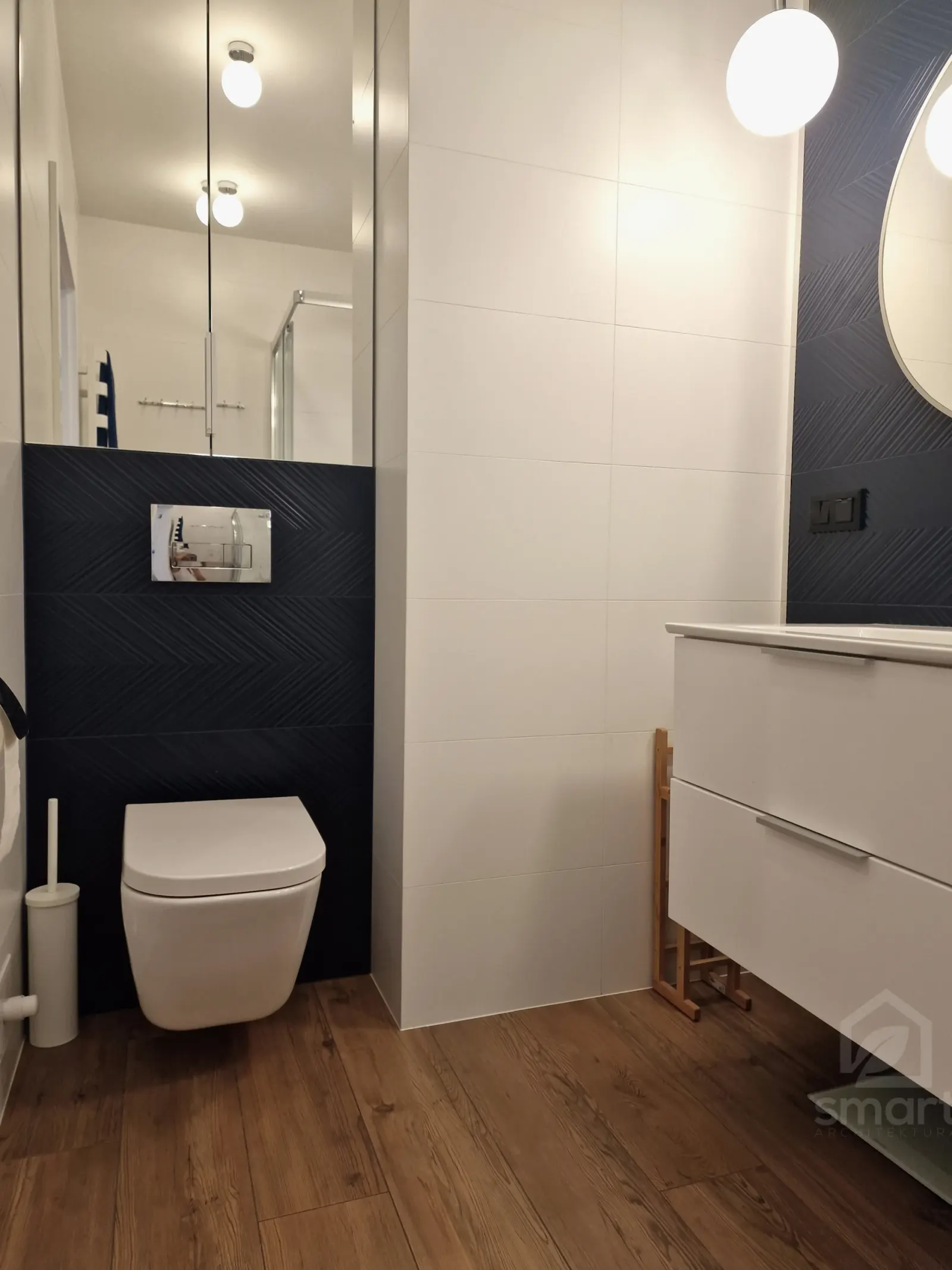 Podwieszana miska WC na tle granatowych płytek i drewnopodobna podłoga