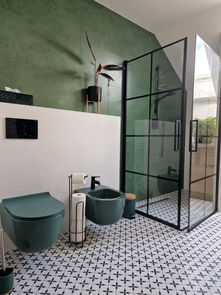 Zielona miska WC i bidet na tle zielonych płytek, obok kabina prysznicowa