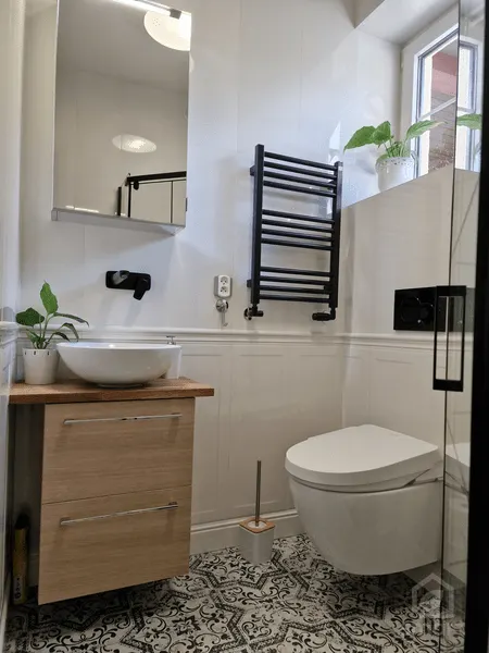 Toaleta z płytkami patchwork na podłodze, drewnianą szafką i czarnym grzejnikiem