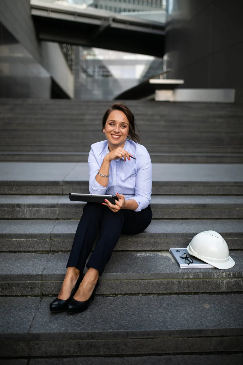 Anna Stawiska, architekt, siedzi na schodach z tabletem, obok kask budowlany
